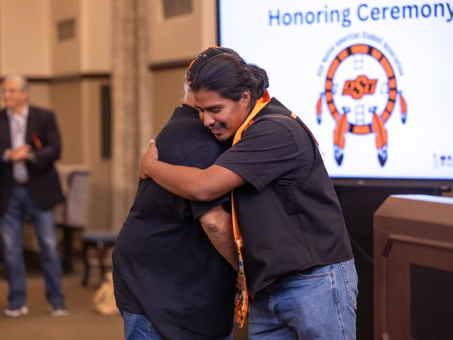 Josiah Kernell shaking hands and hugging elder while wearing a graduation stole