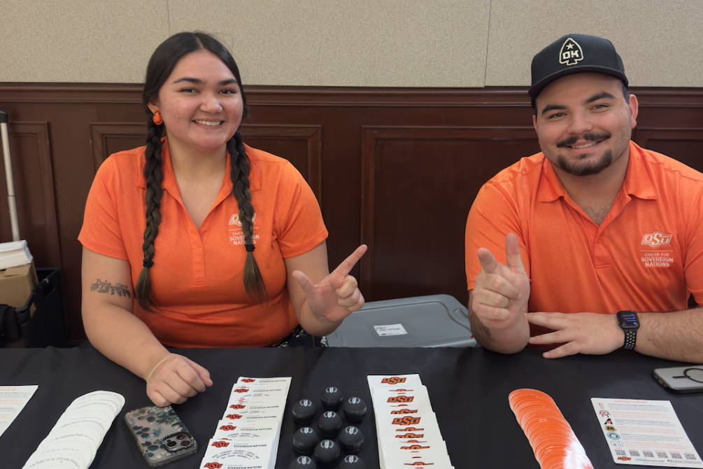 Two students in orange, smiling, showing "Go Pokes" sign