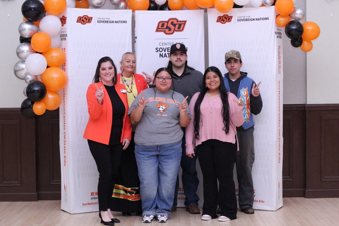 2026-27 NASA EXEC NASA Exec doing the hand signal go pokes in front of white banner and orange black and white balloons