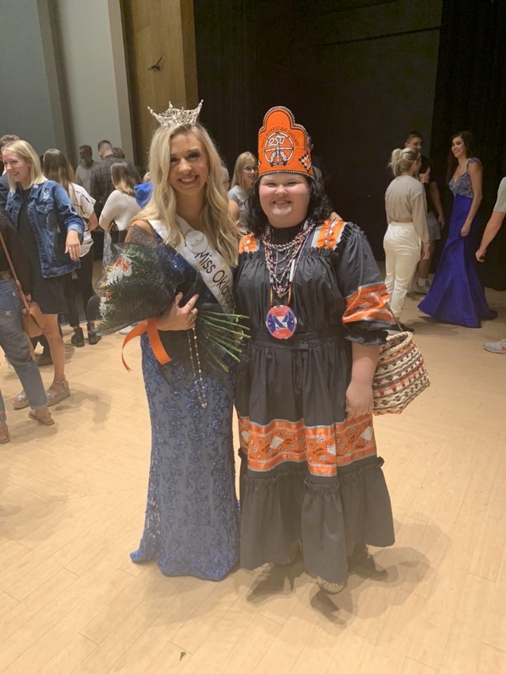 Miss American Indian OSU Kait Pinkerton wearing tradional clothing, and crown posing with Miss Oklahoma State at pagent
