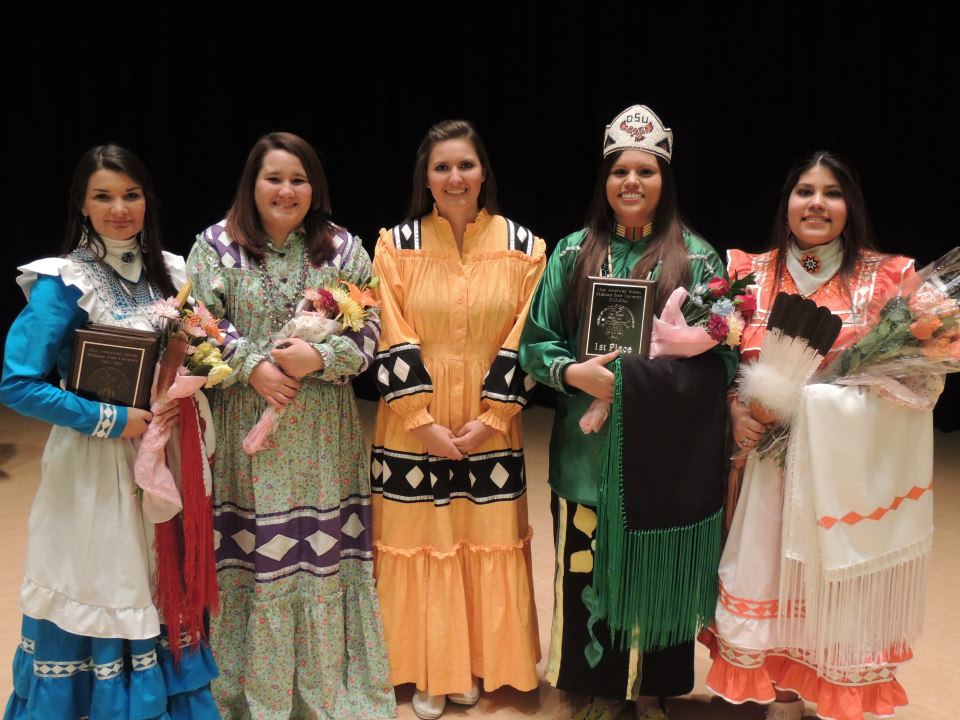 Miss American Indian OSU pictured with other Miss American Indian OSU contestants. All are smiling at the camera, wearing their traditional clothing.