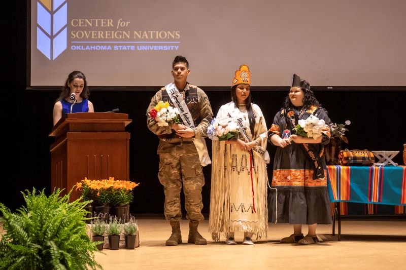 Miss American Indian OSU Gabby and Mister American Indian OSU Luke, newly crowned by former Miss American Indian OSU Kait at the pageant ceremony. Miss Gabby is wearing her tribe’s traditional dress, and Mister Luke is wearing his Army uniform.