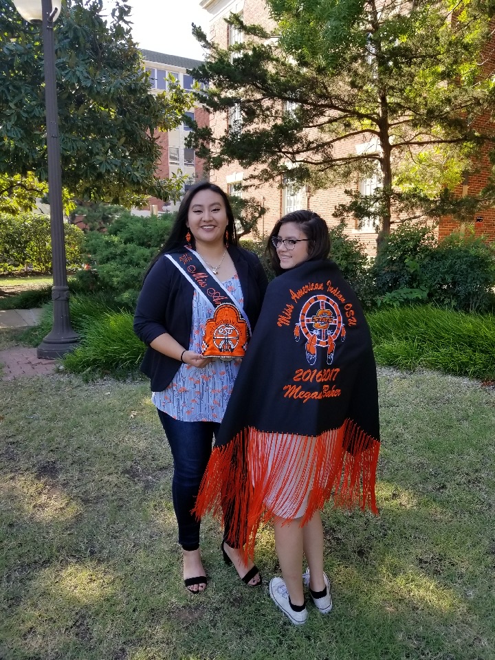 Miss American Indian OSU Cydney pictured with a former Miss American Indian OSU Meg, showing off their crowns, sashes, and shawls.