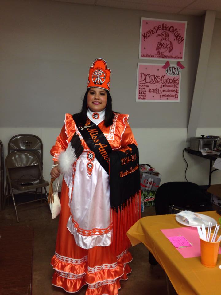 Miss American Indian OSU Veronica pictured wearing orange traditional Choctaw clothing, along with the MAIOSU crown and shawl.