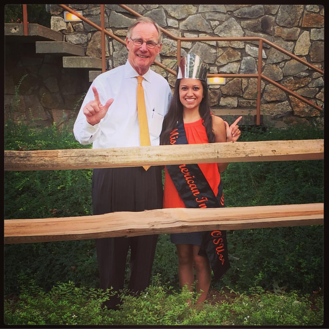 Miss American Indian OSU pictured smiling, wearing the MAIOSU sash, and posing with OSU President Burns Hargis.