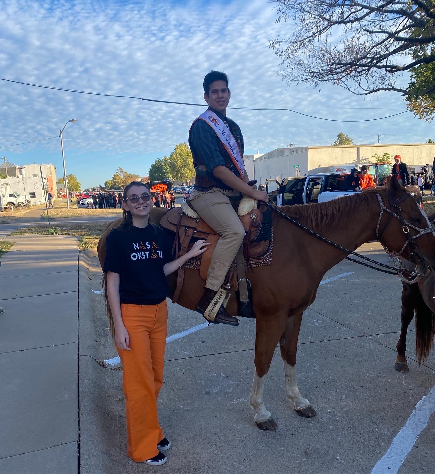 Mr American Indian OSU Luke posing on a horse with NASA Exec Jenna at OSU homecoming paradePictured