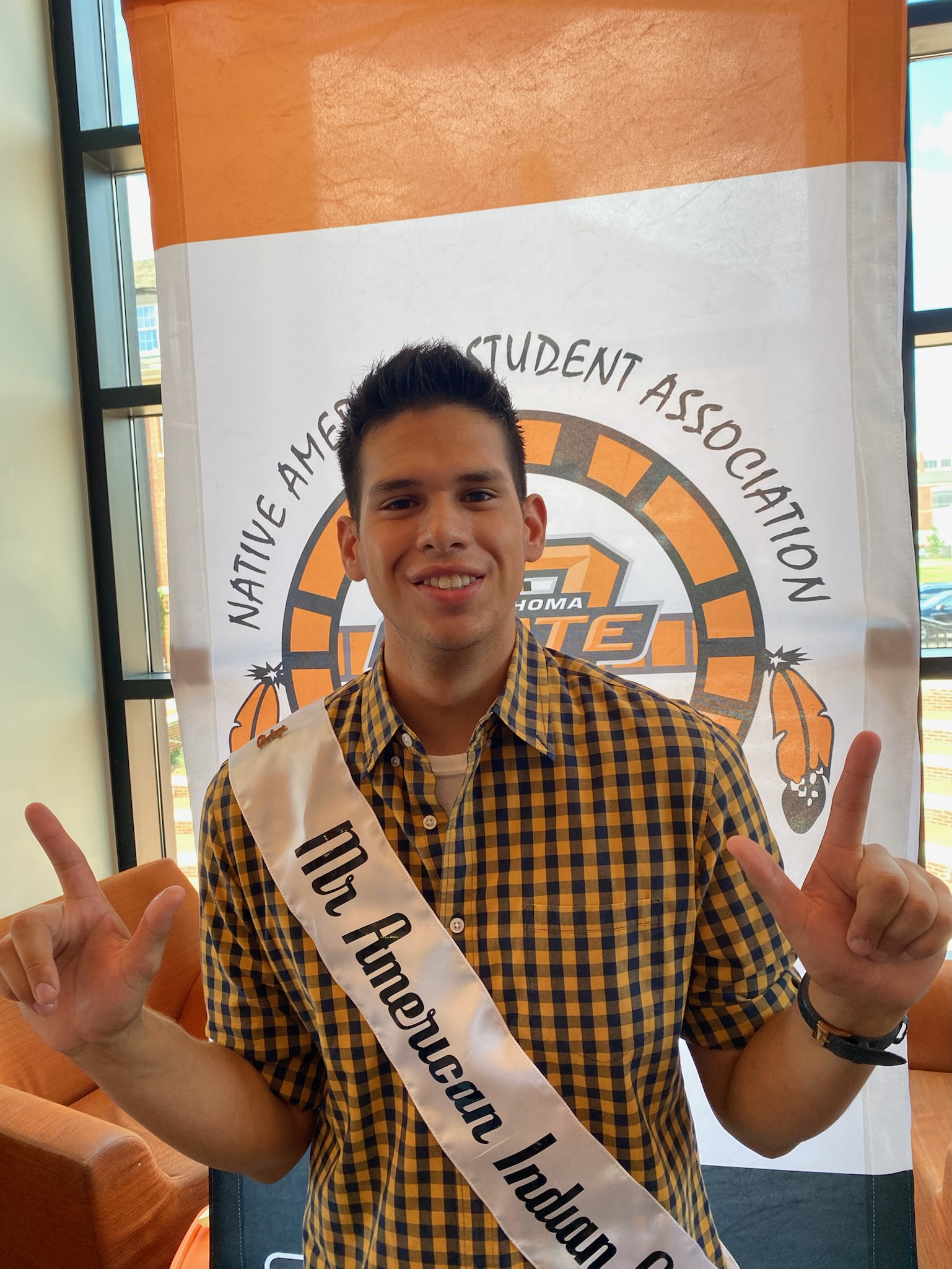 Mister American Indian OSU Luke pictured wearing the MAIOSU sash, standing at a NASA tabling event.