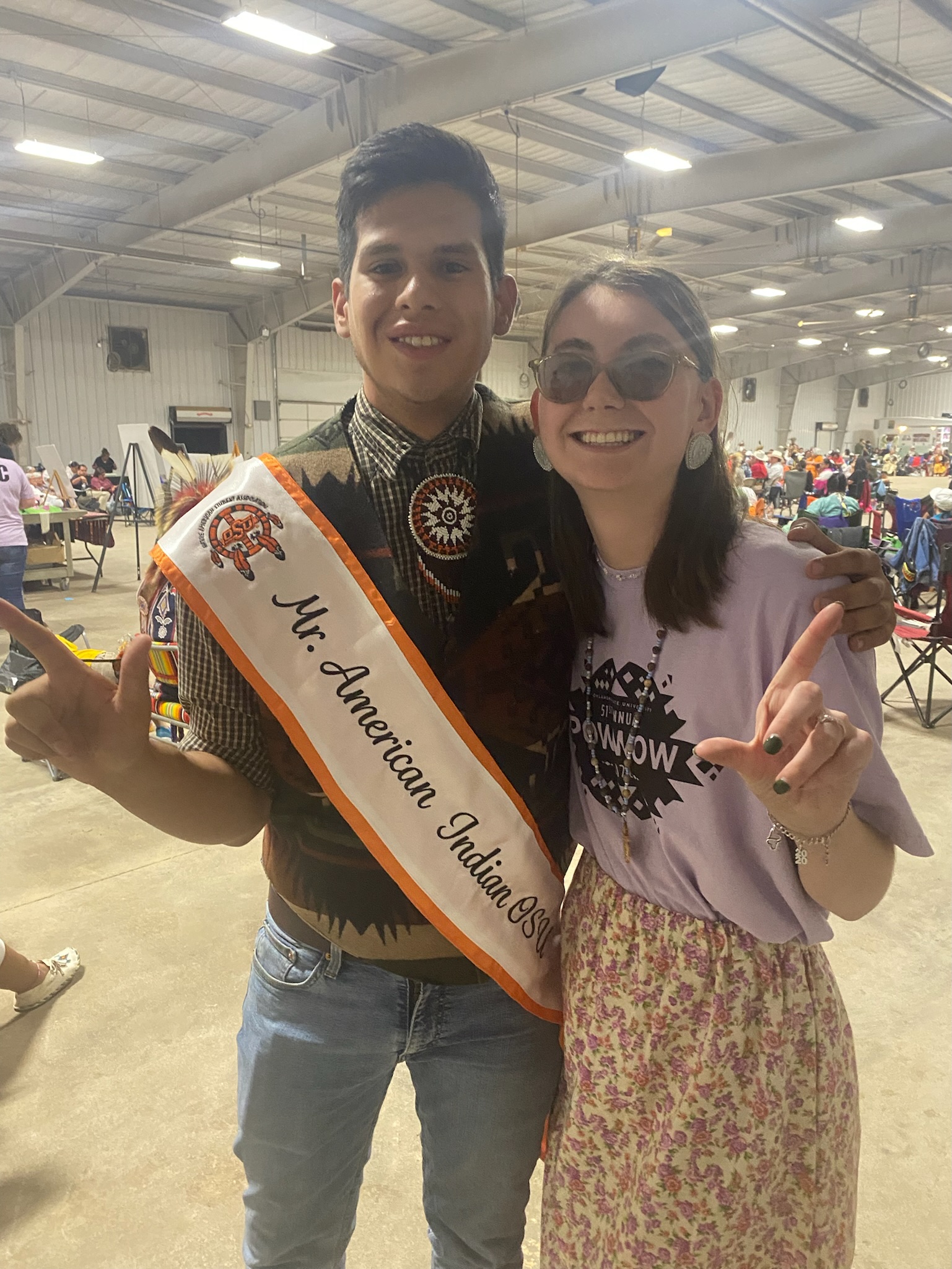 Mr American Indian OSU wearing MAISOU Sash posing with NASA Exec Jenna at OSU Powwow