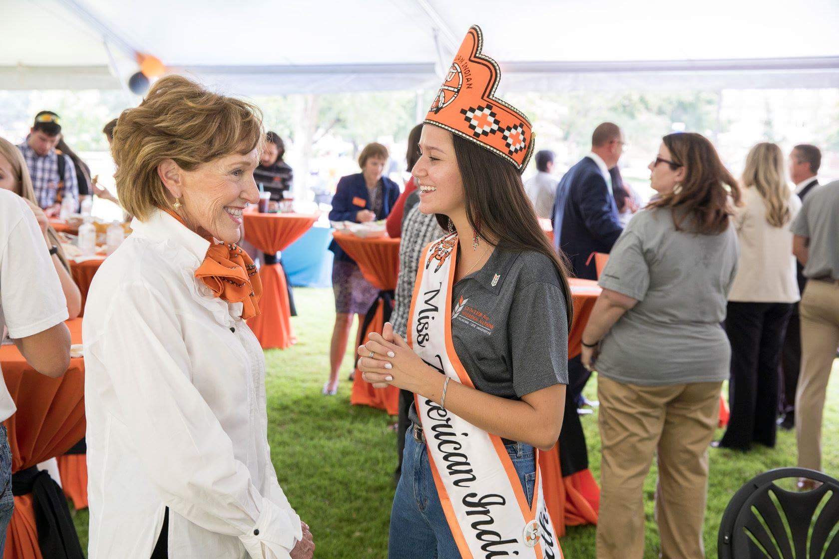 Miss American Indian OSU Cathrine, wearing the MAIOSU crown and sash, speaking to a Center for Sovereign Nations partner at the Center for Sovereign Nations birthday event.