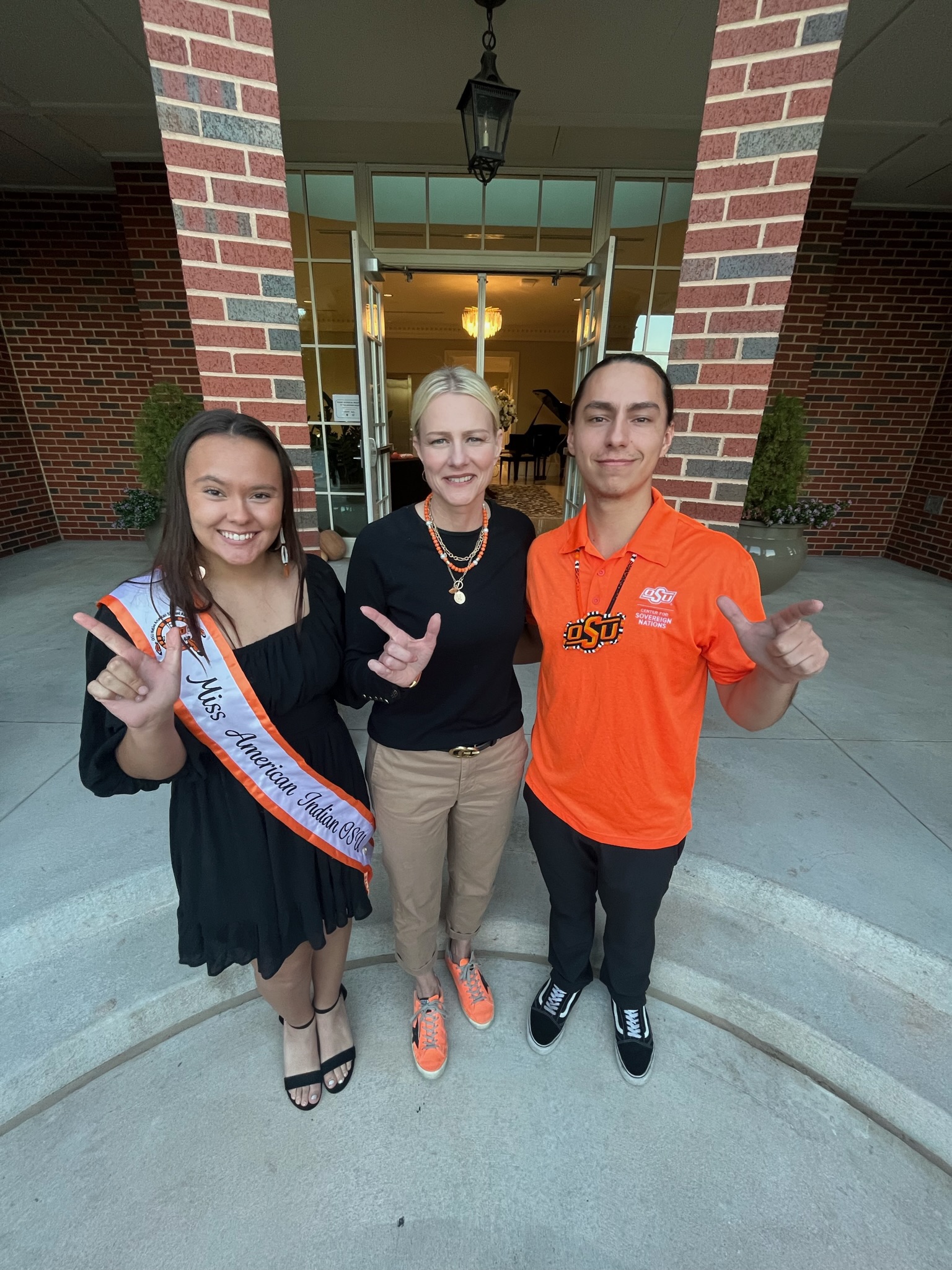 Miss American Indian OSU Shaeleigh and Mister American Indian OSU Caleb, both wearing black, standing with OSU President Kayse Shrum.