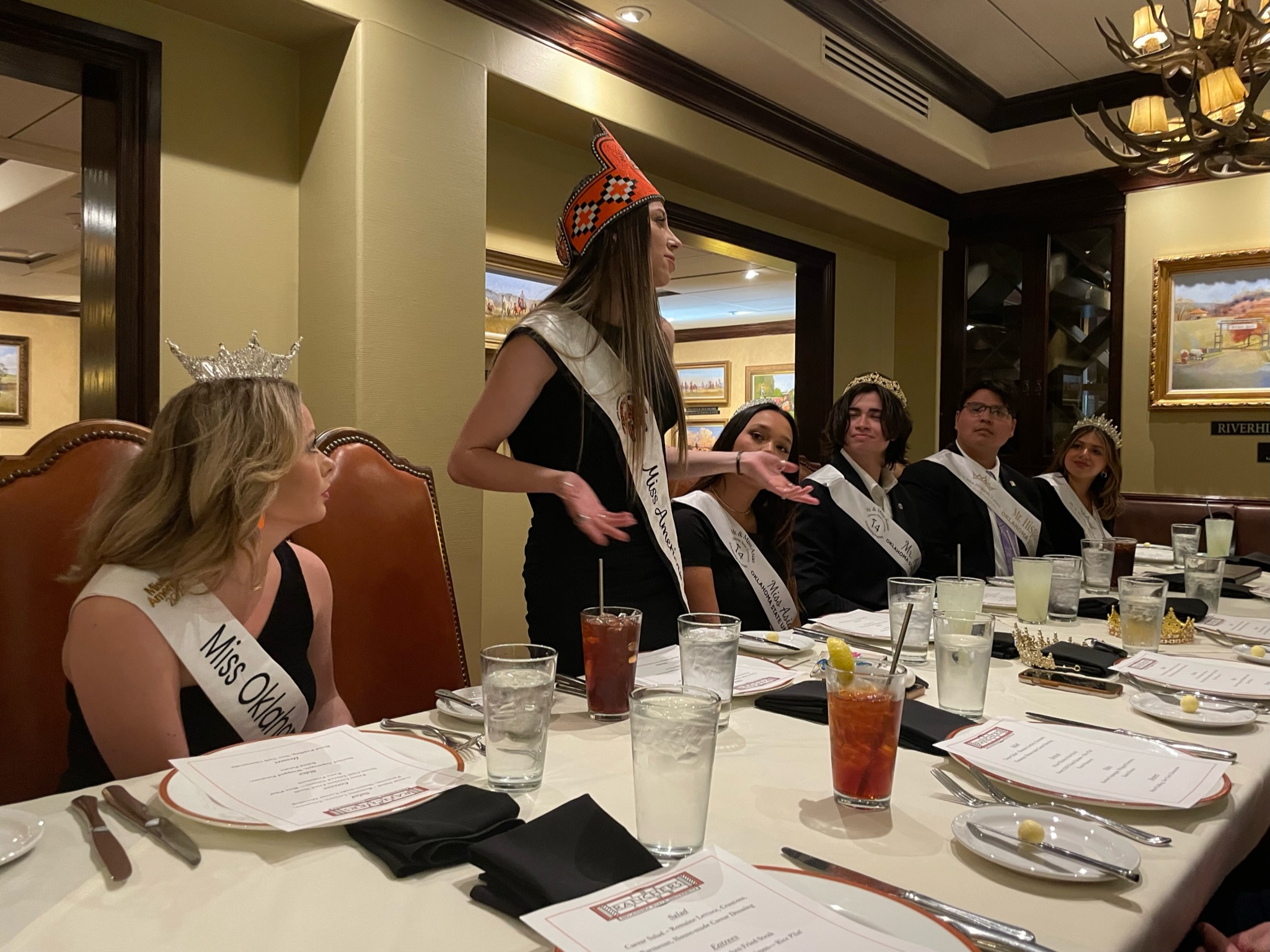 Miss American Indian OSU Lauren pictured standing and speaking at the OSU Royal Dinner with all 2024–2025 OSU royalty.