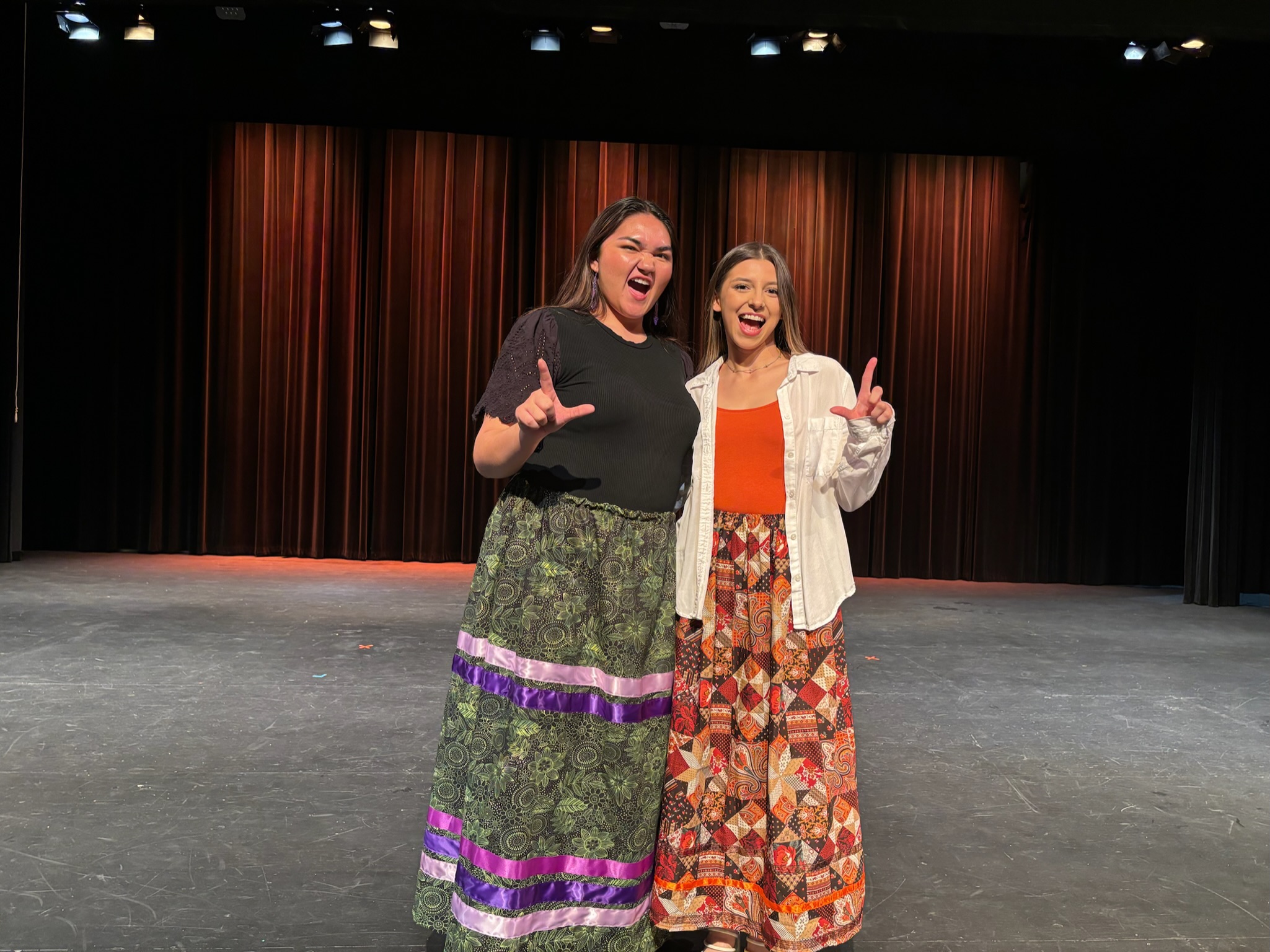 Miss American Indian OSU Lauren pictured with contestant Krysha, both wearing ribbon skirts, smiling at the 2024–2025 MAIOSU pageant.