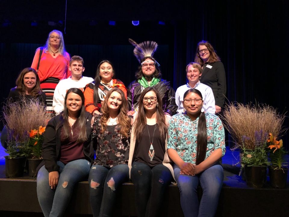 Miss American Indian OSU Cydnee and Mister American Indian OSU Che, wearing sashes and crowns in traditional regalia, smiling with the NASA executive team and co-advisors Dr. Kathern Gage and Dawna Riding-in-Hare, and Center for Sovereign Nations founding director Elizabeth Payne at the MAIOSU pageant.