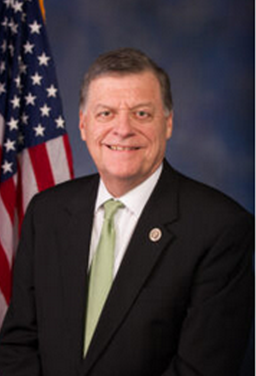 Headshot photo of Tom Cole with a suit on in front of an American Flag.