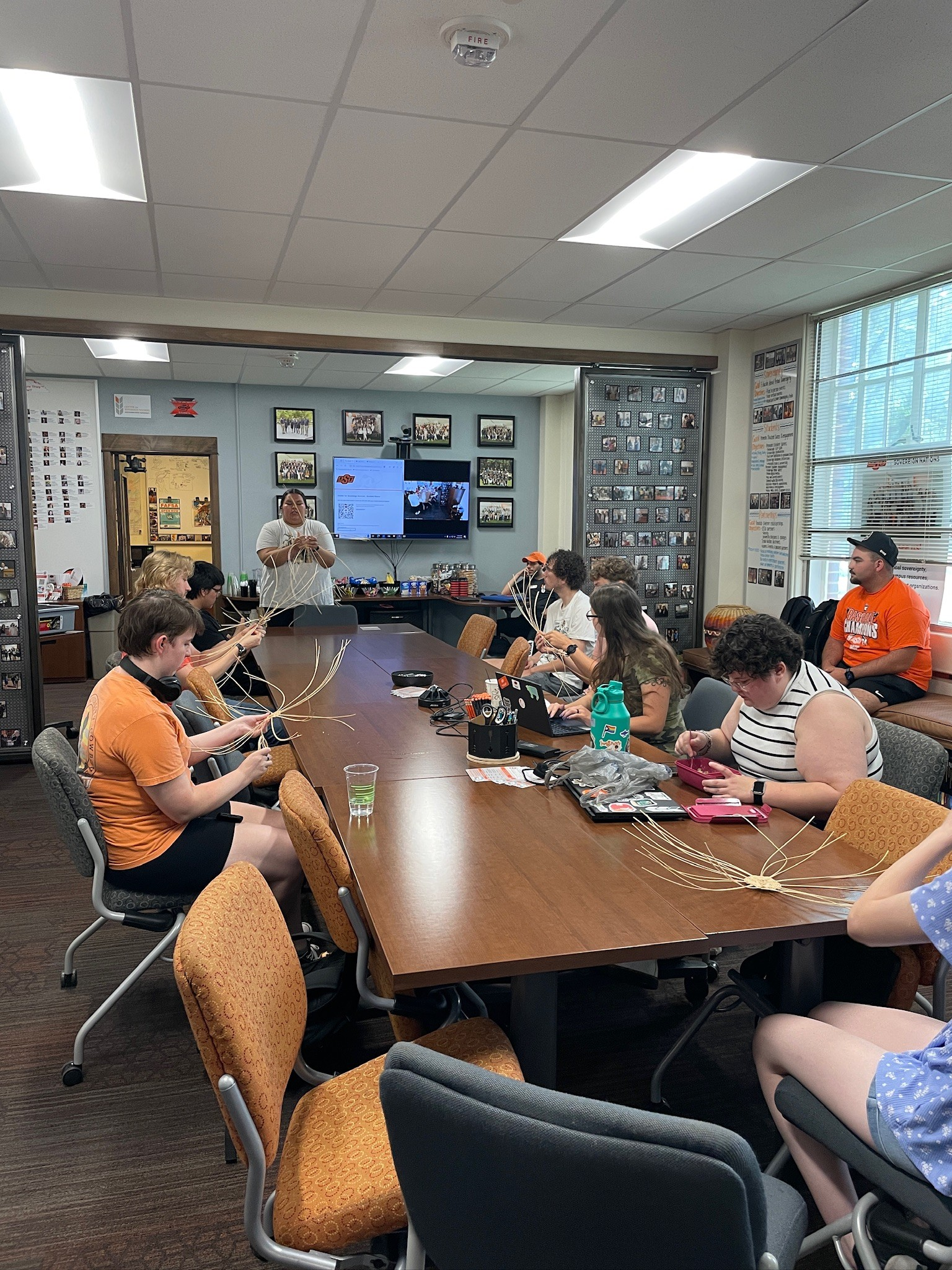 People seated around a table engaged in a basket weaving session in a well-lit room.