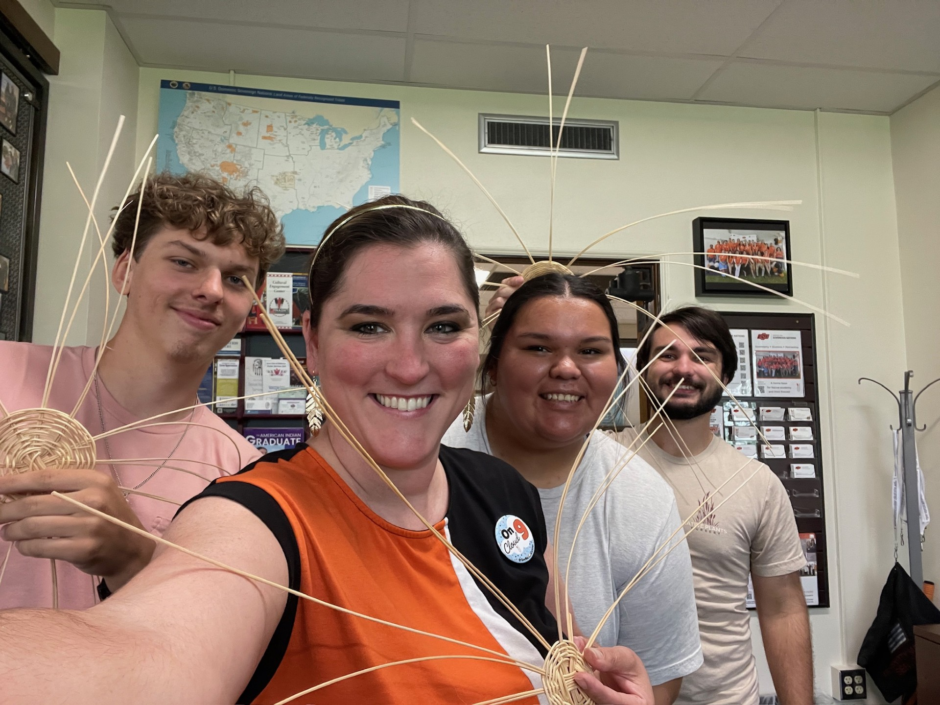 Four people smiling into the camera showing their partially woven baskets.