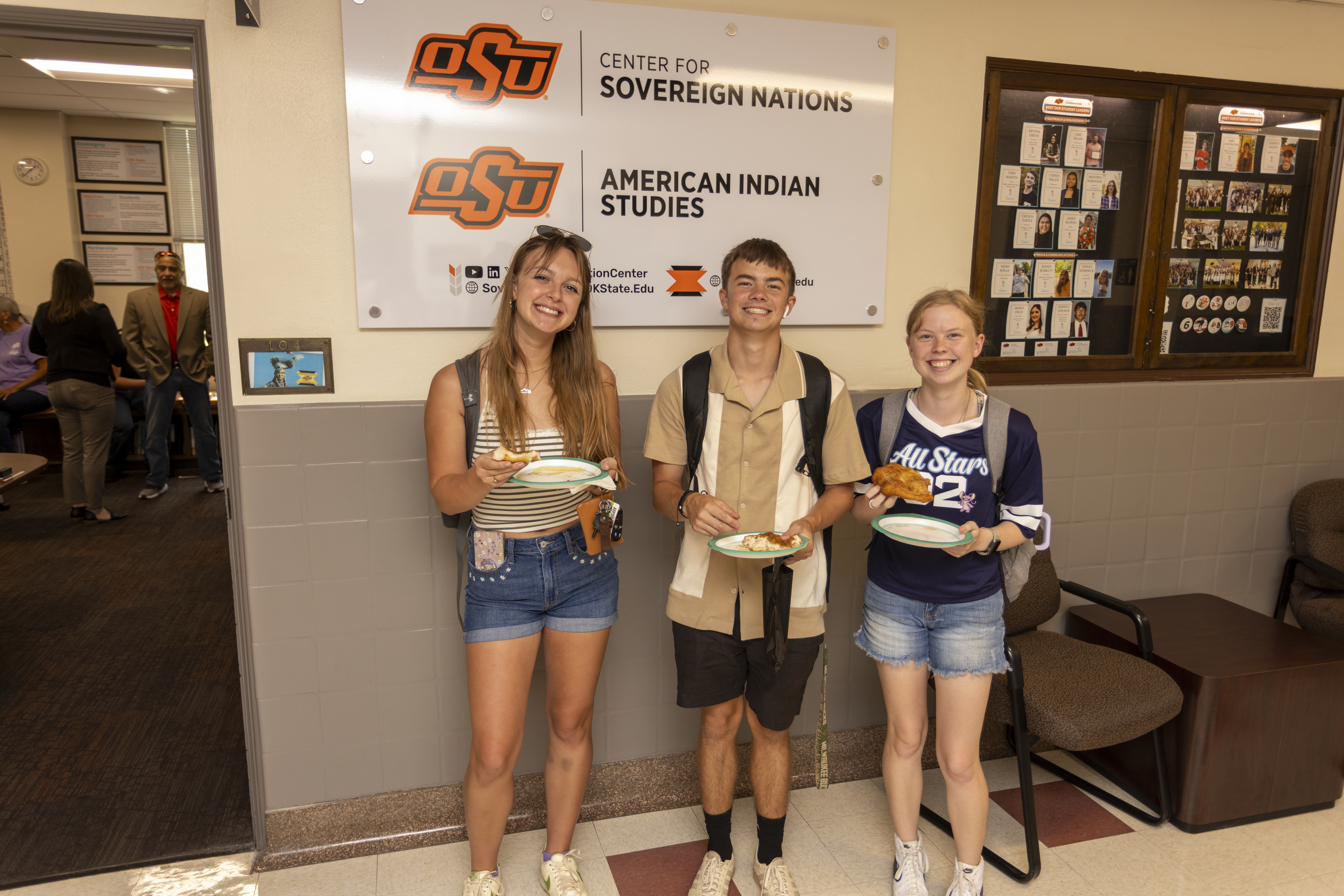 A group of people standing in front of a sign in a hallway holding plates of frybread.